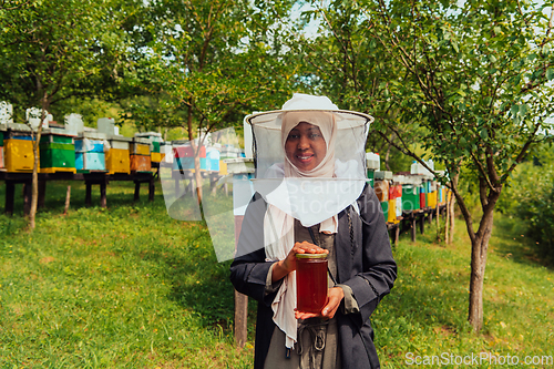 Image of Portrait of a Muslim African American woman in the beekeeping department of a honey farm holding a jar of honey in her hand