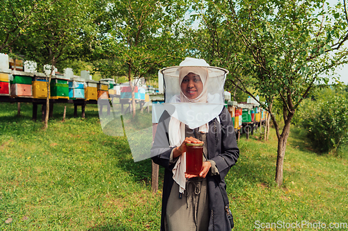 Image of Portrait of a Muslim African American woman in the beekeeping department of a honey farm holding a jar of honey in her hand