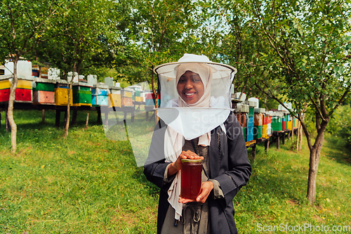 Image of Portrait of a Muslim African American woman in the beekeeping department of a honey farm holding a jar of honey in her hand