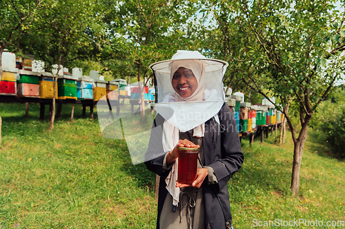 Image of Portrait of a Muslim African American woman in the beekeeping department of a honey farm holding a jar of honey in her hand