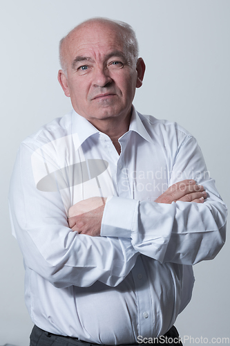 Image of Confident senior man in white shirt crossing hands on chest and looking at camera while standing against gray background. Self confident senior isolated white studio shoot.