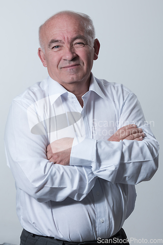 Image of Confident senior man in white shirt crossing hands on chest and looking at camera while standing against gray background. Self confident senior isolated white studio shoot.