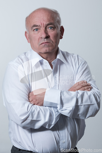 Image of Confident senior man in white shirt crossing hands on chest and looking at camera while standing against gray background. Self confident senior isolated white studio shoot.