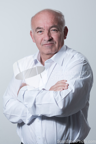 Image of Confident senior man in white shirt crossing hands on chest and looking at camera while standing against gray background. Self confident senior isolated white studio shoot.