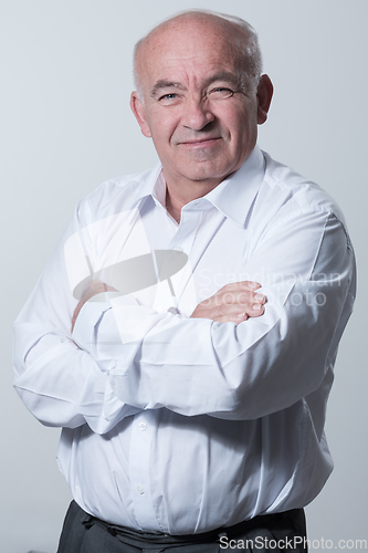 Image of Confident senior man in white shirt crossing hands on chest and looking at camera while standing against gray background. Self confident senior isolated white studio shoot.