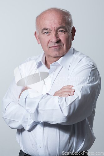 Image of Confident senior man in white shirt crossing hands on chest and looking at camera while standing against gray background. Self confident senior isolated white studio shoot.