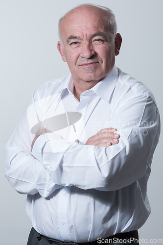 Image of Confident senior man in white shirt crossing hands on chest and looking at camera while standing against gray background. Self confident senior isolated white studio shoot.