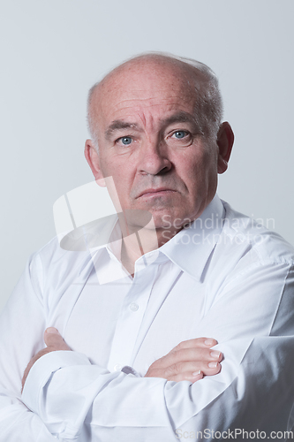 Image of Confident senior man in white shirt crossing hands on chest and looking at camera while standing against gray background. Self confident senior isolated white studio shoot.