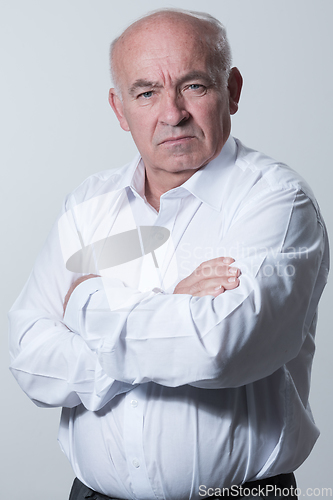 Image of Confident senior man in white shirt crossing hands on chest and looking at camera while standing against gray background. Self confident senior isolated white studio shoot.