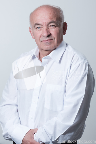 Image of Portrait of an older man wearing a white shirt on a gray background. A healthy old man looks at a camera isolated over a gray wall. An older man smiles at the camera, a happy old man.