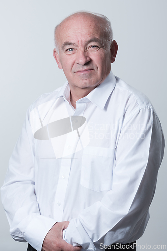 Image of Portrait of an older man wearing a white shirt on a gray background. A healthy old man looks at a camera isolated over a gray wall. An older man smiles at the camera, a happy old man.