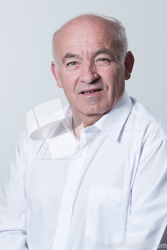 Image of Portrait of an older man wearing a white shirt on a gray background. A healthy old man looks at a camera isolated over a gray wall. An older man smiles at the camera, a happy old man.