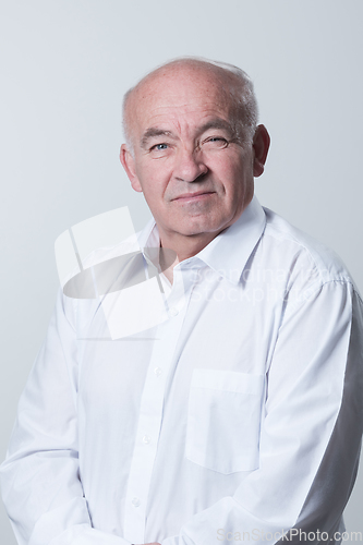 Image of Portrait of an older man wearing a white shirt on a gray background. A healthy old man looks at a camera isolated over a gray wall. An older man smiles at the camera, a happy old man.