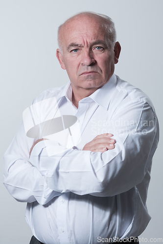 Image of Confident senior man in white shirt crossing hands on chest and looking at camera while standing against gray background. Self confident senior isolated white studio shoot.