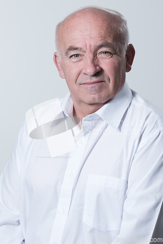 Image of Portrait of an older man wearing a white shirt on a gray background. A healthy old man looks at a camera isolated over a gray wall. An older man smiles at the camera, a happy old man.