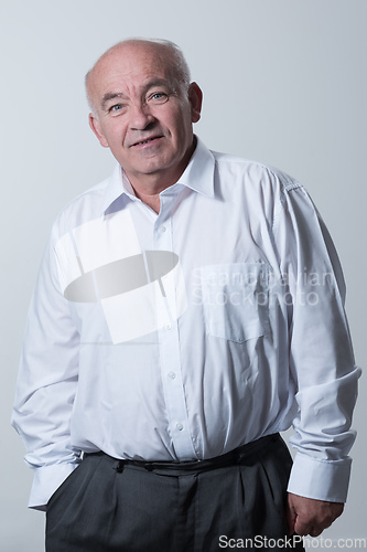 Image of Portrait of an older man wearing a white shirt on a gray background. A healthy old man looks at a camera isolated over a gray wall. An older man smiles at the camera, a happy old man.