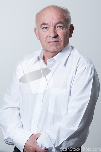 Image of Portrait of an older man wearing a white shirt on a gray background. A healthy old man looks at a camera isolated over a gray wall. An older man smiles at the camera, a happy old man.