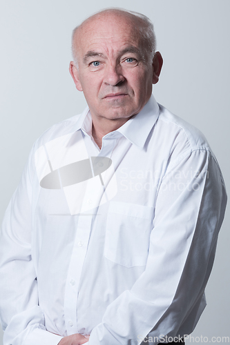 Image of Portrait of an older man wearing a white shirt on a gray background. A healthy old man looks at a camera isolated over a gray wall. An older man smiles at the camera, a happy old man.