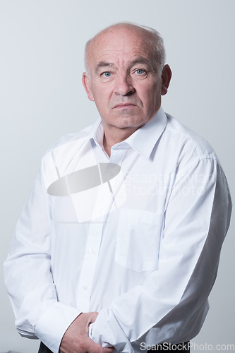 Image of Portrait of an older man wearing a white shirt on a gray background. A healthy old man looks at a camera isolated over a gray wall. An older man smiles at the camera, a happy old man.