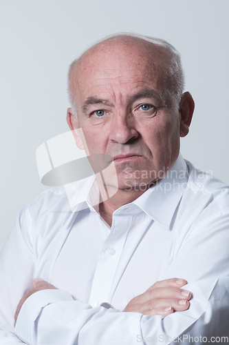 Image of Confident senior man in white shirt crossing hands on chest and looking at camera while standing against gray background. Self confident senior isolated white studio shoot.