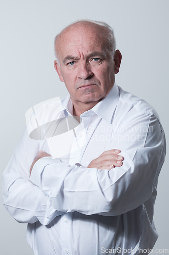 Image of Confident senior man in white shirt crossing hands on chest and looking at camera while standing against gray background. Self confident senior isolated white studio shoot.