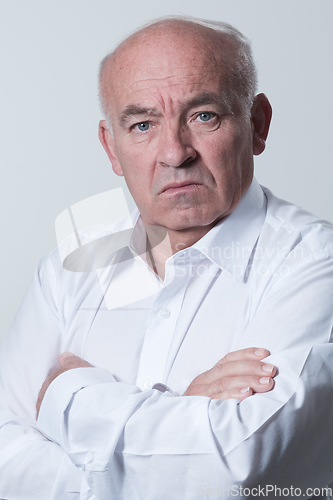 Image of Confident senior man in white shirt crossing hands on chest and looking at camera while standing against gray background. Self confident senior isolated white studio shoot.