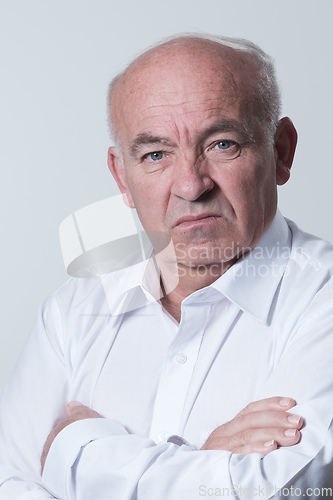 Image of Confident senior man in white shirt crossing hands on chest and looking at camera while standing against gray background. Self confident senior isolated white studio shoot.