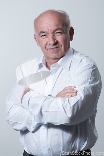 Image of Confident senior man in white shirt crossing hands on chest and looking at camera while standing against gray background. Self confident senior isolated white studio shoot.