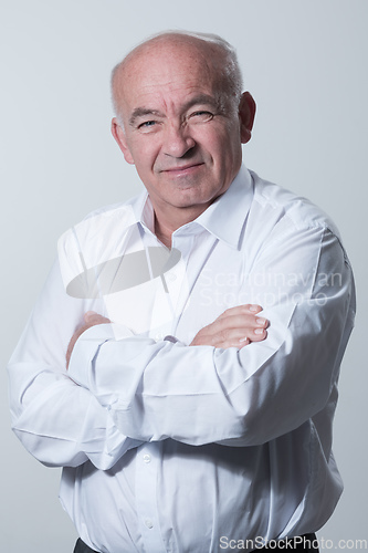 Image of Confident senior man in white shirt crossing hands on chest and looking at camera while standing against gray background. Self confident senior isolated white studio shoot.