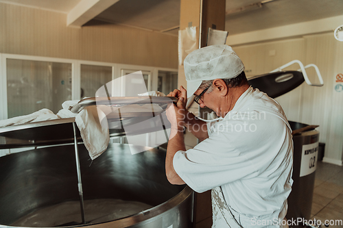 Image of Man mixing milk in the stainless tank during the fermentation process at the cheese manufacturing