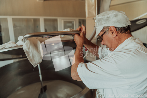 Image of Man mixing milk in the stainless tank during the fermentation process at the cheese manufacturing