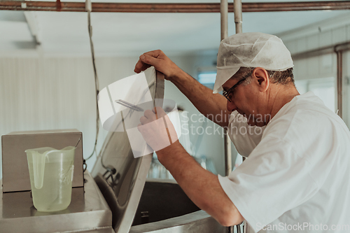 Image of Man mixing milk in the stainless tank during the fermentation process at the cheese manufacturing