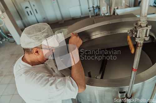 Image of Man mixing milk in the stainless tank during the fermentation process at the cheese manufacturing