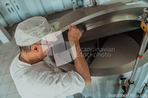 Image of Man mixing milk in the stainless tank during the fermentation process at the cheese manufacturing