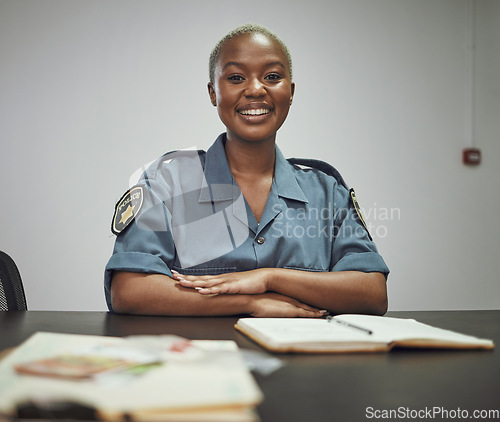 Image of Happy, smile and portrait of a female police officer sitting by a desk in the office writing reports. Confidence, happiness and African woman security guard with a positive mindset in the workplace.