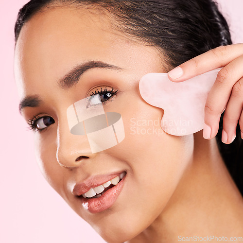 Image of Natural beauty, face massage and woman with a gua sha, skin glow and cosmetics. Portrait of a young aesthetic female model happy with self care, facial or dermatology results on a pink background