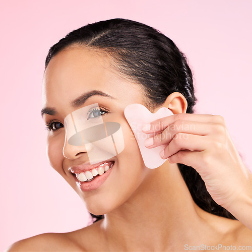 Image of Facial massage, natural beauty and woman with a gua sha, skin glow and cosmetics. Face of a young aesthetic female model happy with self care and dermatology stone results on a pink background