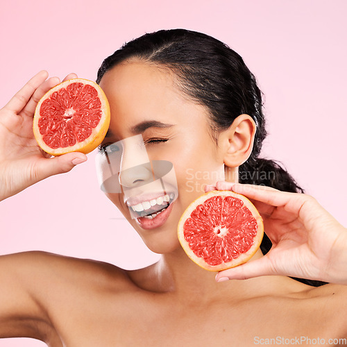 Image of Face, beauty and woman wink with grapefruit in studio isolated on a pink background. Portrait, natural cosmetic and model with fruit, food or nutrition for skincare, healthy vegan diet or vitamin c