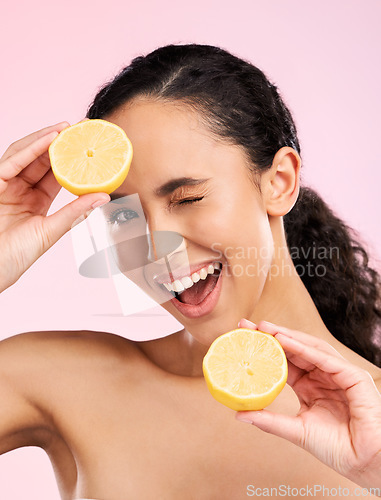 Image of Woman, beauty and lemon for wink in studio portrait, smile and natural skin glow by pink background. Latino girl, model and fruit for cosmetics, eye emoji and detox for wellness, nutrition and shine