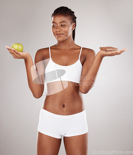 Image of Choice, apple and black woman with chocolate for health decision and isolated in gray studio background with junk food. Balance, wellness and African person holding fruit and sweet, dessert or candy