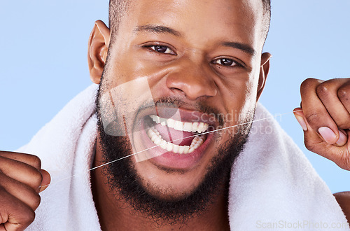 Image of Portrait, man and floss teeth in studio, health dental and self care of gum gingivitis. Face of black male model, thread or cleaning mouth for fresh breath, tooth hygiene or plaque on blue background