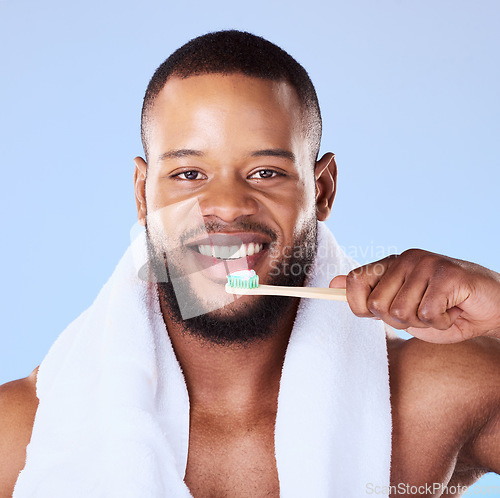 Image of Portrait, black man and brushing teeth in studio for dental, bamboo toothbrush and blue background. Face of male model cleaning mouth with eco friendly wooden product for fresh breath or oral hygiene