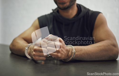 Image of Man, criminal and handcuffs for interrogation, crime or money laundering in arrest on table in room. Closeup of male person, gangster or suspect in jail, justice or guilty for fraud, theft or scam