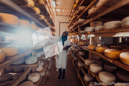 Image of African American Muslim businesswoman checking product quality and entering data into a laptop at a local cheese manufacturing company