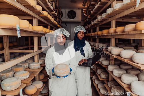 Image of Business of a Muslim partners in a cheese warehouse, checking the quality of cheese and entering data into laptop