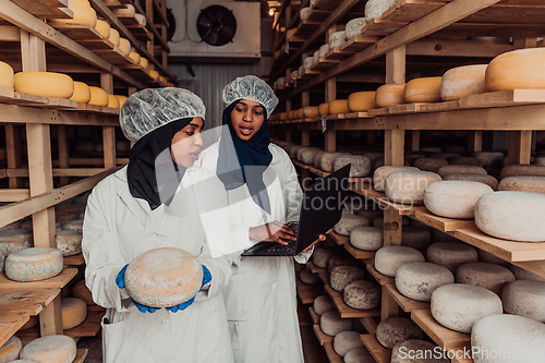 Image of Business of a Muslim partners in a cheese warehouse, checking the quality of cheese and entering data into laptop