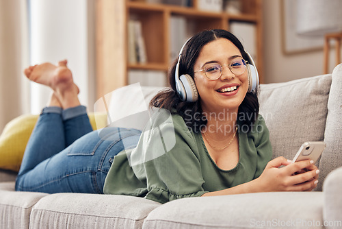 Image of Woman, portrait and headphones with smartphone on sofa, for hearing radio, online subscription and podcast. Happy female person listening to music, streaming audio and sound on mobile in living room