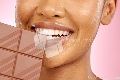 Image of Woman, mouth and chocolate in studio closeup with smile, eating and skin glow for beauty by pink background. Girl, model and diet with sweets, snack or candy for cheat day, cosmetics and headshot