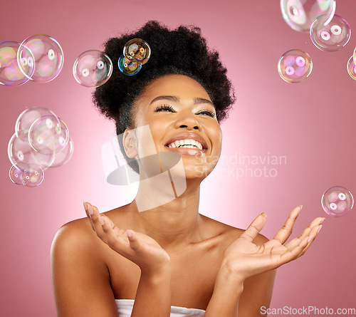 Image of Beauty, bubbles and a happy woman with skin care in studio for wellness and dermatology glow. Happy, natural makeup and face cosmetics of a black female model with facial shine on a pink background