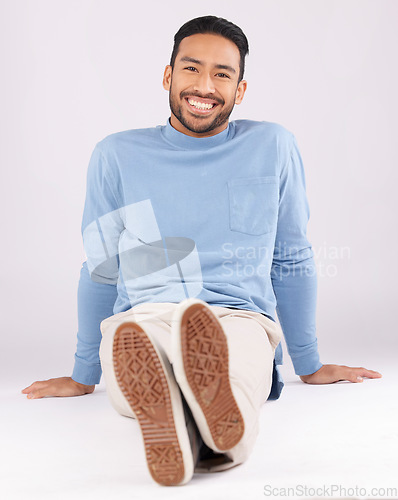 Image of Portrait, fashion and man smile on the floor in studio isolated on a white background. Style, happy and Asian person from Cambodia in casual clothes, trendy aesthetic or confidence to relax on ground